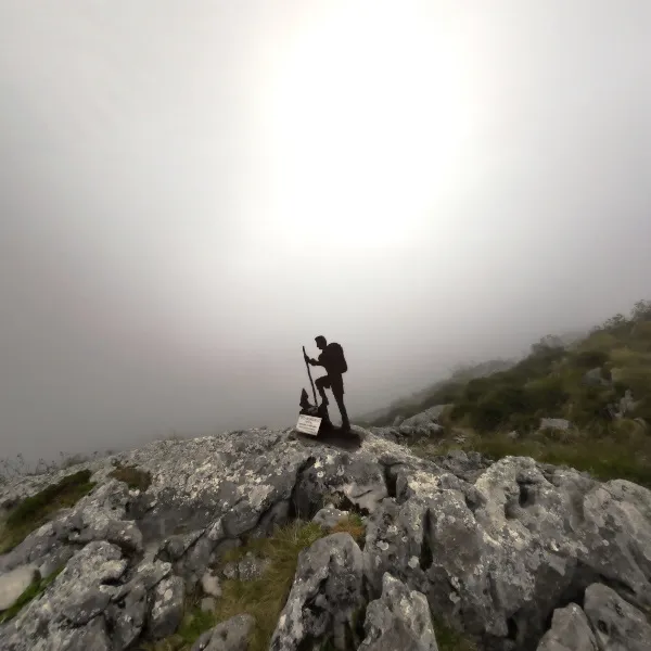 Cima del Pico Mancuevu con escultura de montañero entre la niebla